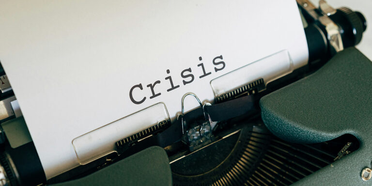 Green typewriter with white paper with only the word "Crisis" on it