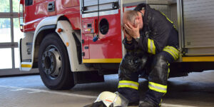 Firefighter appearing distressed sitting on side of fire truck.