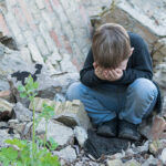 Sad, little boy near destroyed house.
